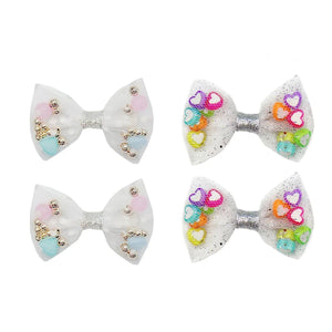 A set of hairclips featuring mesh tulle bows with glitter trim and pockets filled with tiny beads and hearts in multicolor.
