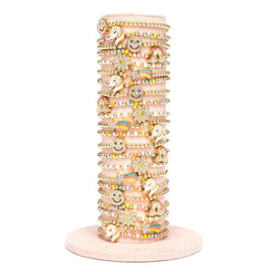 A stack of multicolored beaded bracelets with cute animal and smiley face charms, presented on a pink stand.