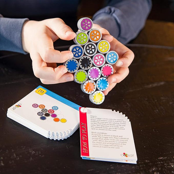 Colorful gears held by a person with game cards and instructions on a wooden surface