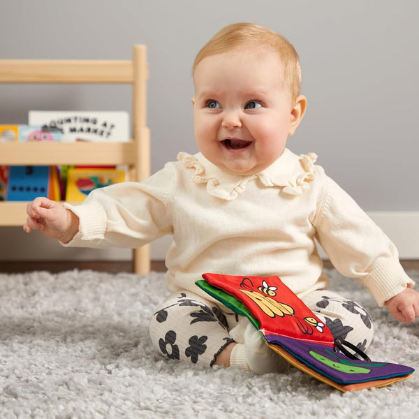 Baby playing with a colorful toy on a carpeted floor in a room with books and toys.