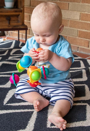 Baby playing with a colorful toy on a patterned rug.