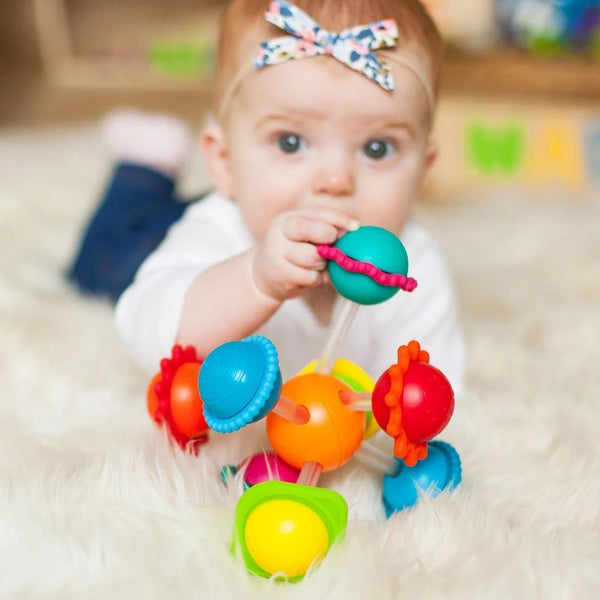 Baby playing with a colorful teething toy on a soft surface
