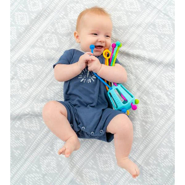 Baby holding colorful toys on a textured white blanket