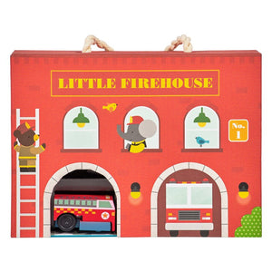 A cardboard playset depicting a firehouse with a wind-up fire engine and track pieces.