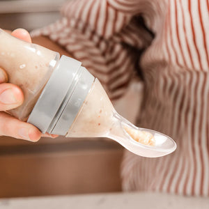 Person holding a baby food puree container with a spoon filled with food
