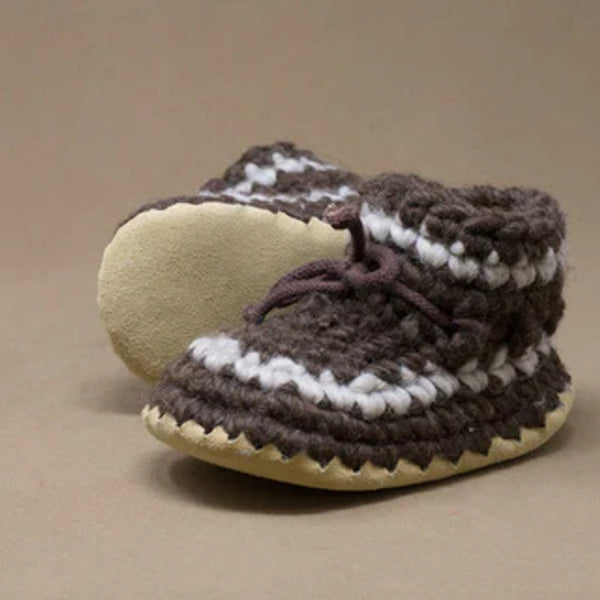 Pair of brown and white crocheted baby shoes on a beige background