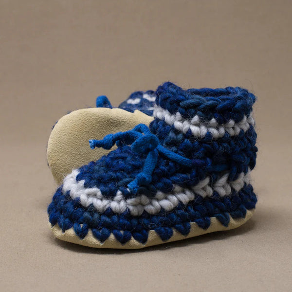 Pair of blue and white crocheted baby booties on a beige background