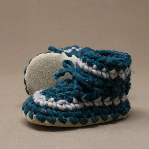 Pair of blue and white baby booties on a beige background