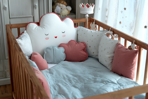 Children's crib with cloud-shaped pillow and various decorative pillows in a nursery setting.